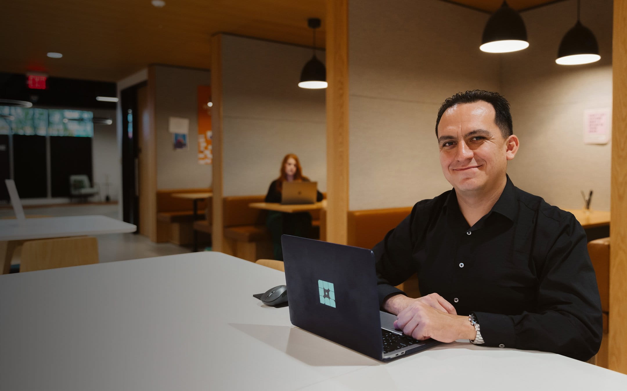 Man in black button-down shirt smiling with a laptop on his desk