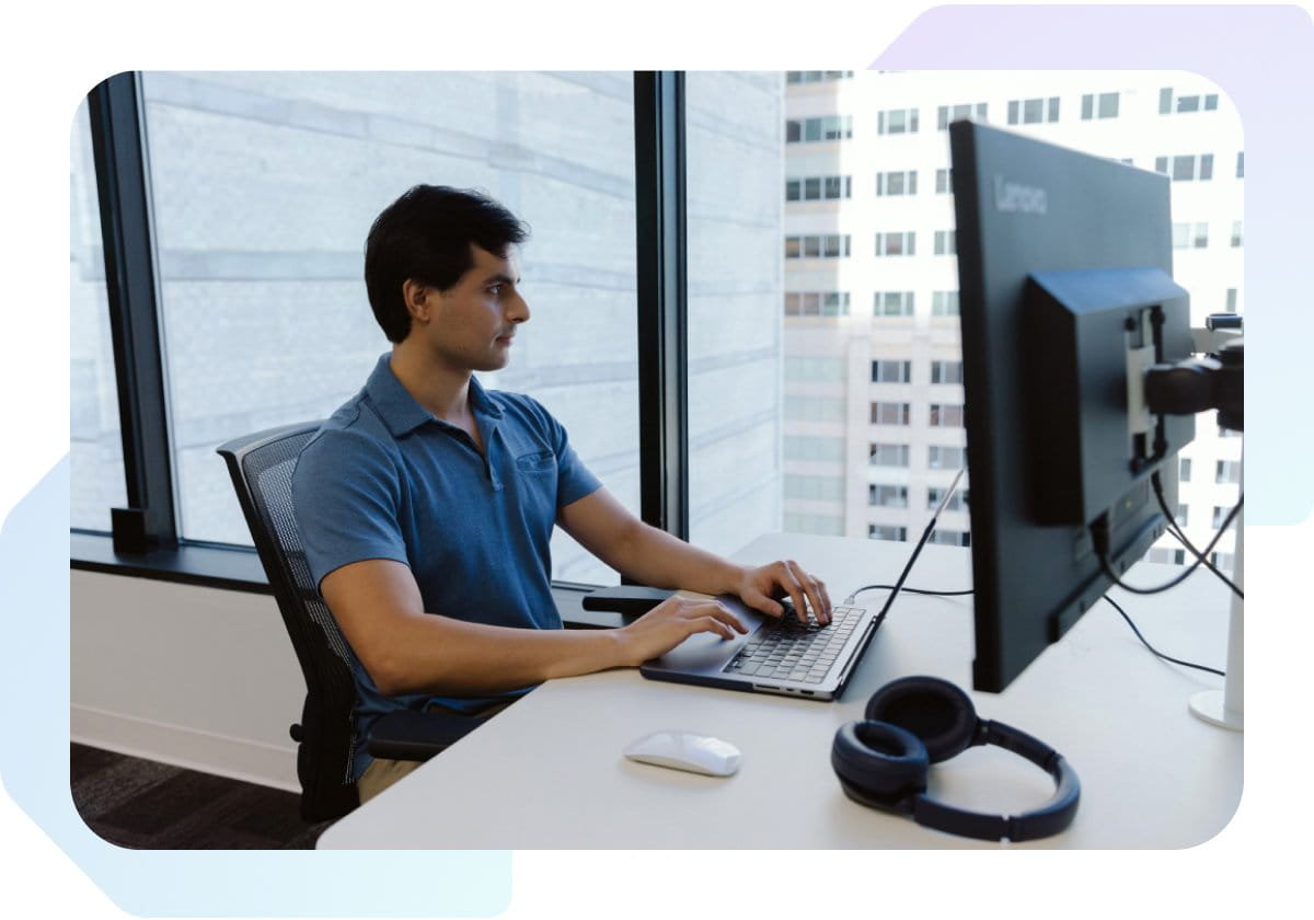 Man in blue polo sitting at a desk looking at a monitor