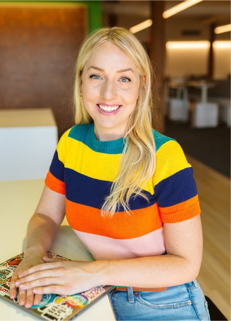 Woman with colorful shirt holds her closed laptop while smiling